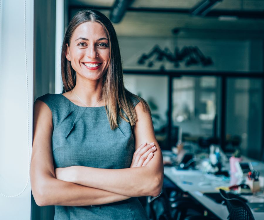 Smiling woman leaning against a wall with a board room in background.