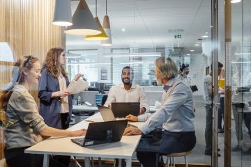 Group of professionals having a meeting in a modern office, with laptops and documents on the table, behind glass walls