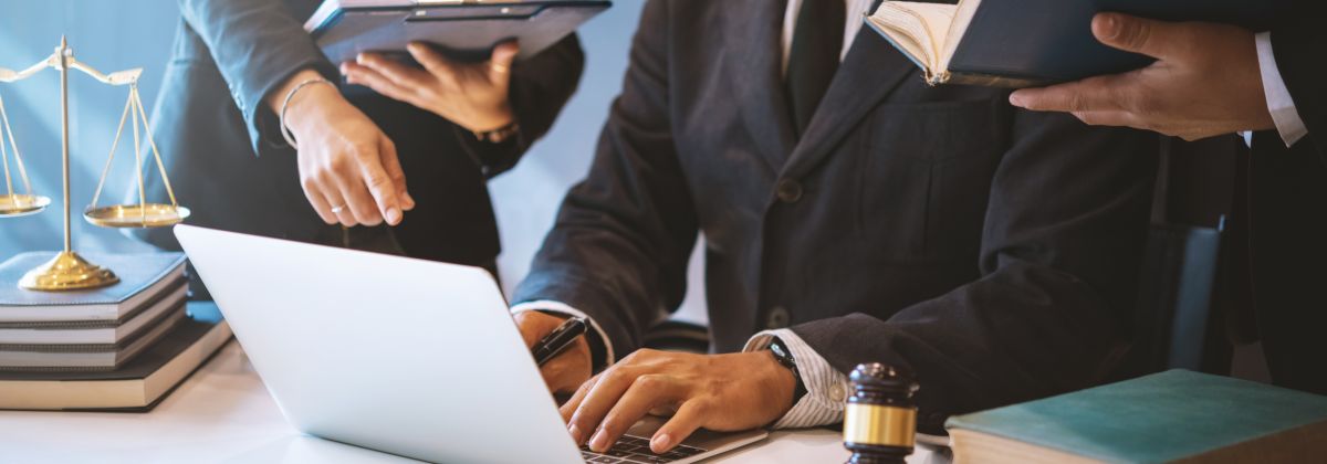 Business professionals in suits working on a laptop with legal books, scales of justice, and a gavel on the table.